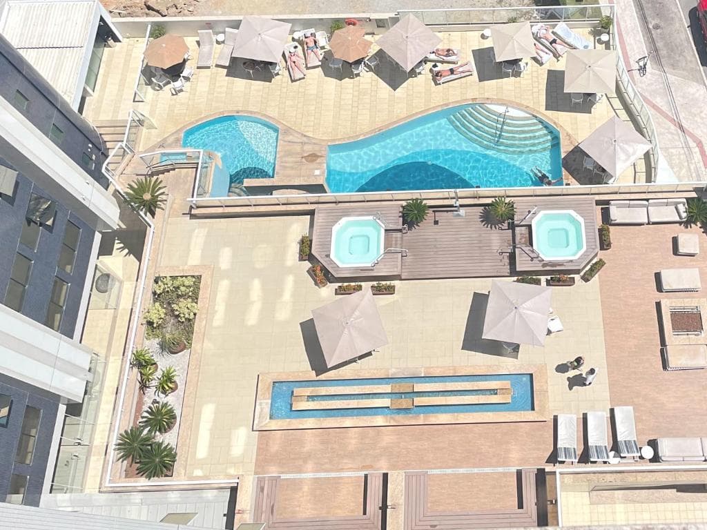 Vista aérea de uma área de lazer luxuosa com piscinas, jacuzzis, guarda-sóis e espreguiçadeiras.
