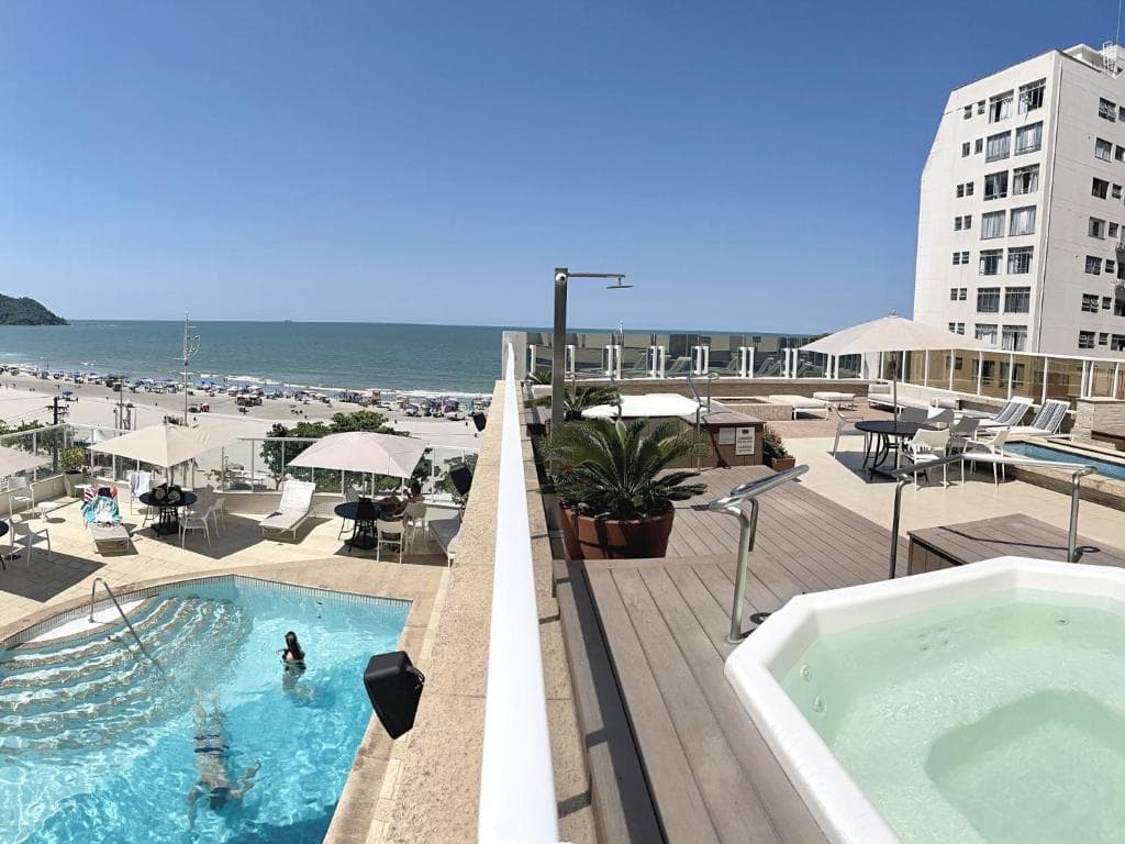 Terraço com piscinas e hidromassagem com vista panorâmica para a praia e o mar azul.