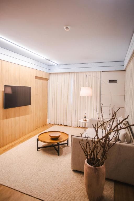 Sala de estar moderna com painel de madeira, TV, sofá bege, mesa redonda e tapete.
